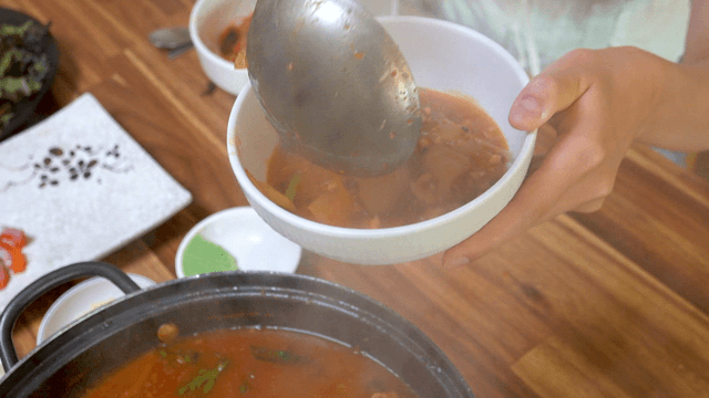 Ladle serving spicy fish stew with hand-pulled dough