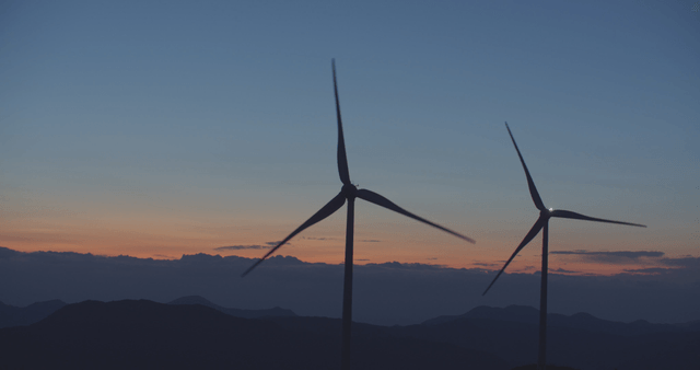 산 너머 일몰의 빠르게 돌아가는 풍력 터빈