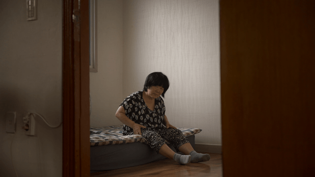 Elderly woman massaging her leg while sitting on a bed