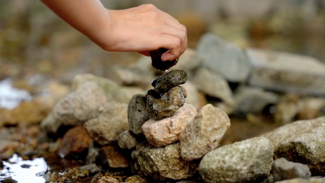A hand stacking stones by a stream
