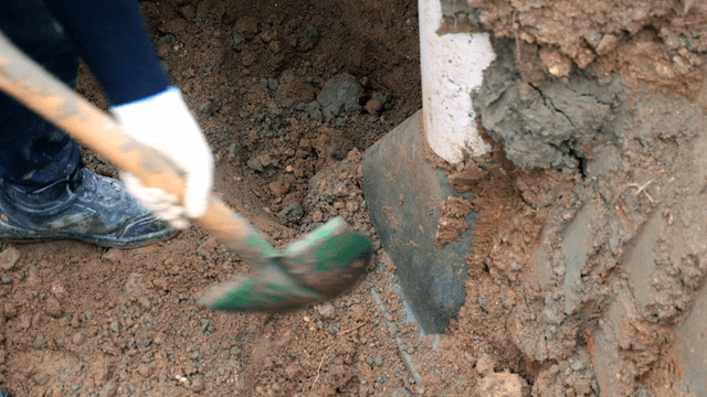 Worker digging soil near a pipe