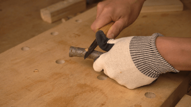 Hands carving wood pieces with a knife on workbench