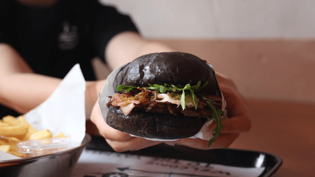 Person holding black burger in restaurant