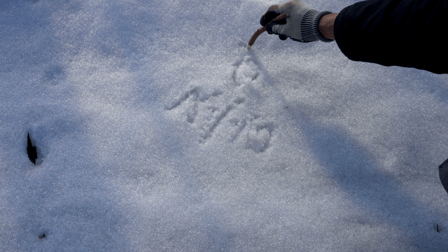 Hand writing on snow with a pencil-shaped wooden stick