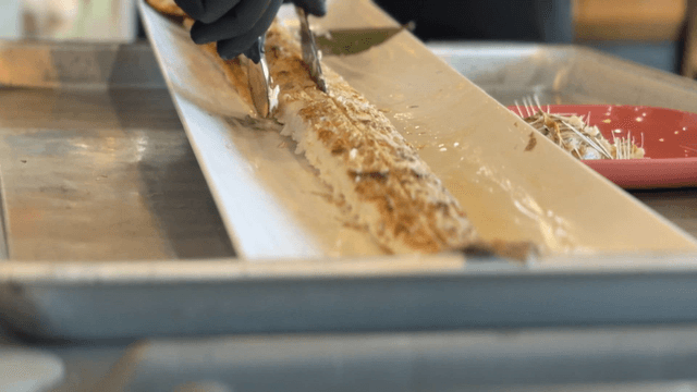 Gloved hands trimming boneless grilled cutlassfish