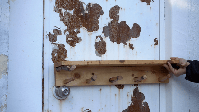Hand placing a wooden stand on a rusty door