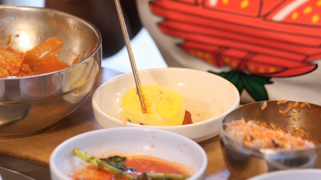Chopsticks holding a piece of rolled omelette