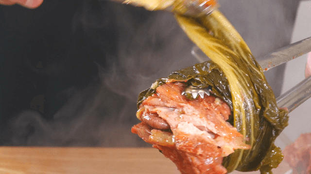 Tongs wrapping boneless pork back-bone meat with outer leaves