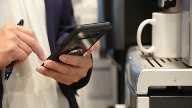 Person using a smartphone near a coffee machine