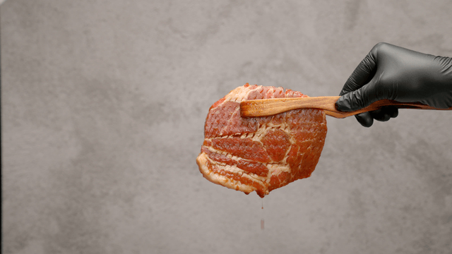 Piece of raw marinated pork held with tongs