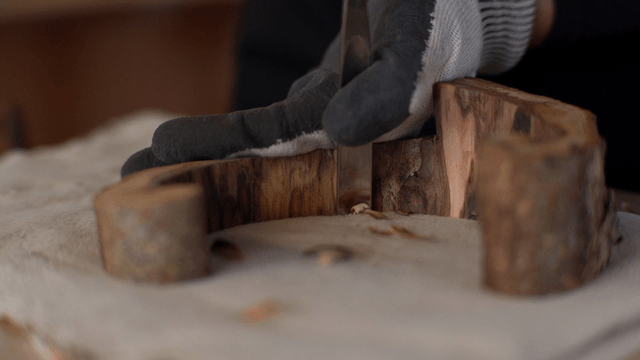Hands carving wood with a chisel while wearing gloves
