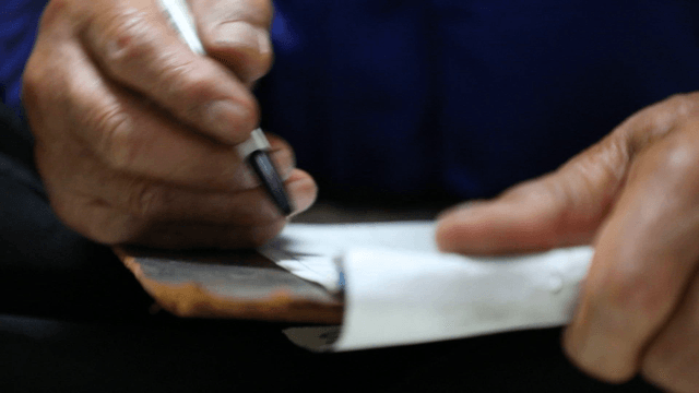 Elderly person writing indoors on a bill