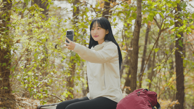 Young woman taking selfie on bench in autumn forest