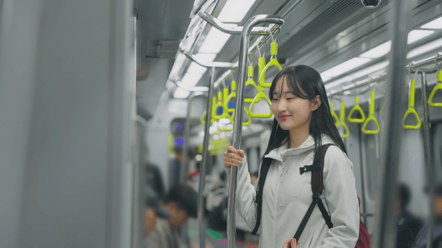 Young woman standing in subway holding seat pole