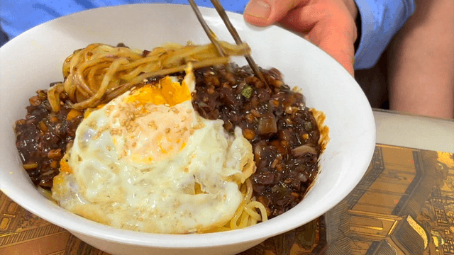 Mixing jajangmyeon with fried egg in rich black bean sauce