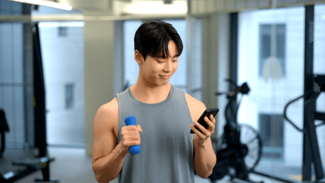 Man smiling at phone while doing dumbbell exercise in gym