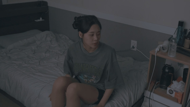 Woman sitting frustrated on her bed in a dark room stands up