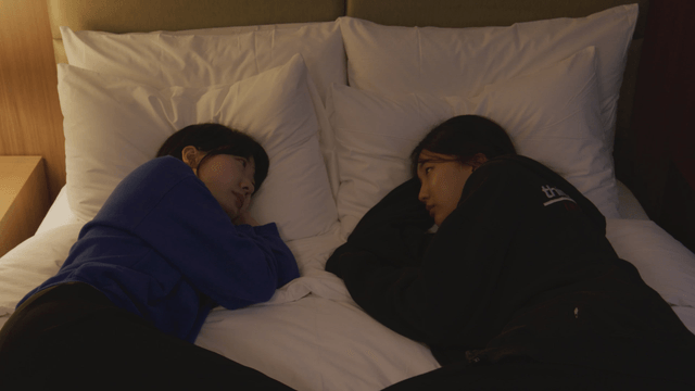 Two figures lying face to face on bed