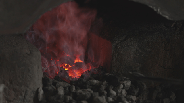 Worker handling glowing charcoal in brazier
