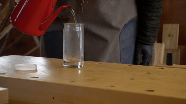 Pouring hot water into a glass bottle on a workbench