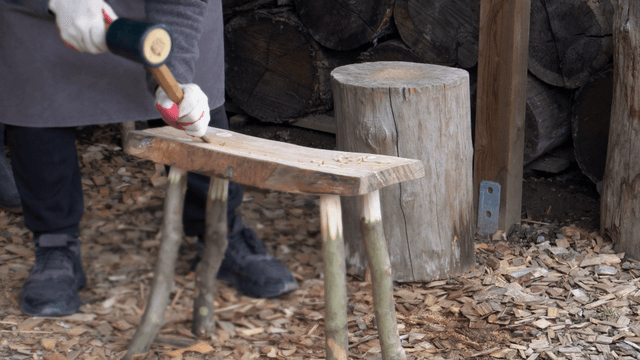 Person crafting a wooden stool outdoors