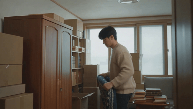 Man tidying bedding in a room with boxes and books
