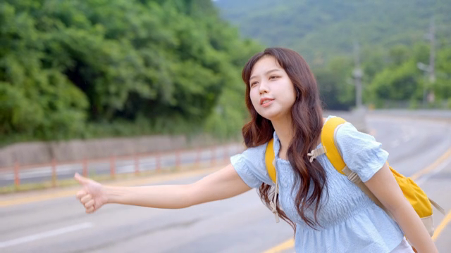 시골 도로에서 히치하이킹하는 젊은 여성