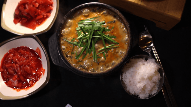 Table set with loach soup, hot stone pot rice, and Korean banknotes