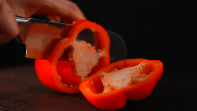 Red bell pepper being sliced on a board