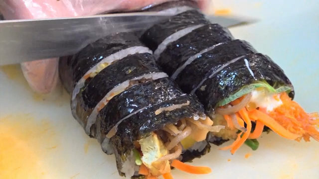 Gimbap being sliced on a cutting board