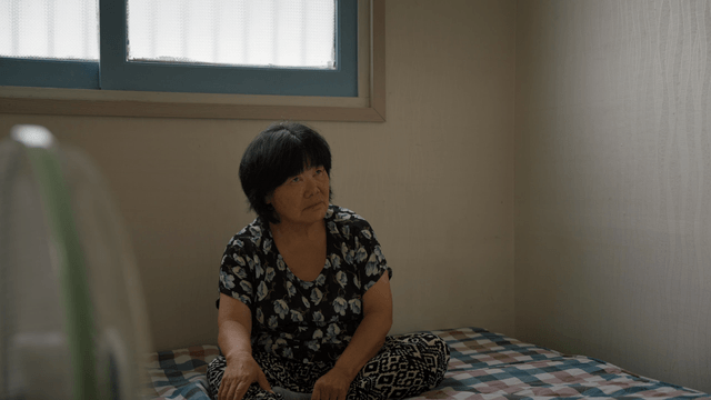 An elderly woman sitting on a bed indoors