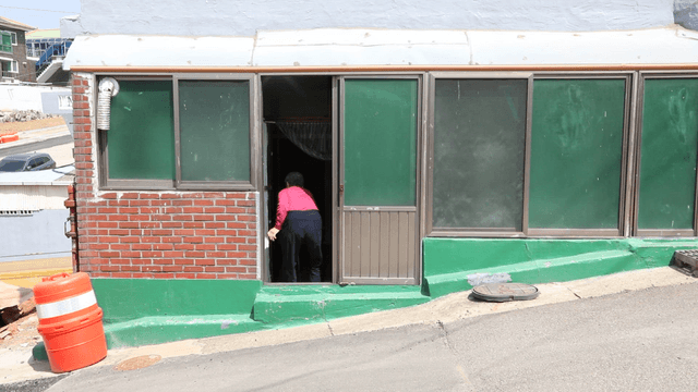 Elderly woman entering a brick house