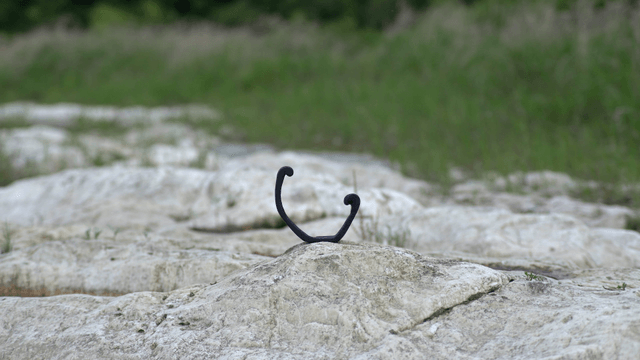 Black hook-shaped wooden sculpture on large white rock