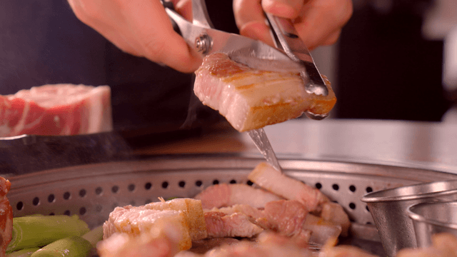 Grilled pork belly being cut with scissors