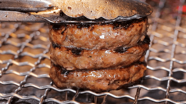 Tongs pressing grilled short rib patties as juice bursts out