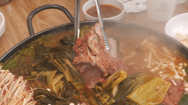Tongs breaking tender pork back-bone meat in outer leaves stew