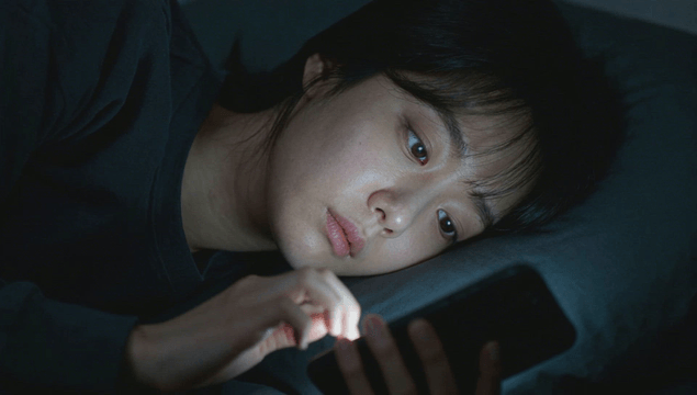 Tired woman using a smartphone while lying on bed at late night