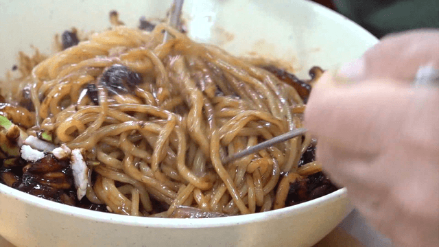 Warm black bean noodles mixed with chopsticks in a bowl