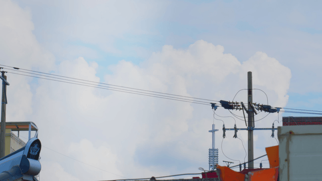 Power lines and a church cross under a cloudy sky