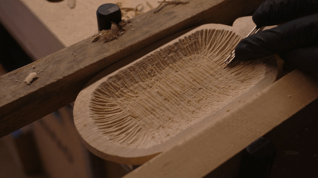 Hands crafting a wooden piece with intricate pattern