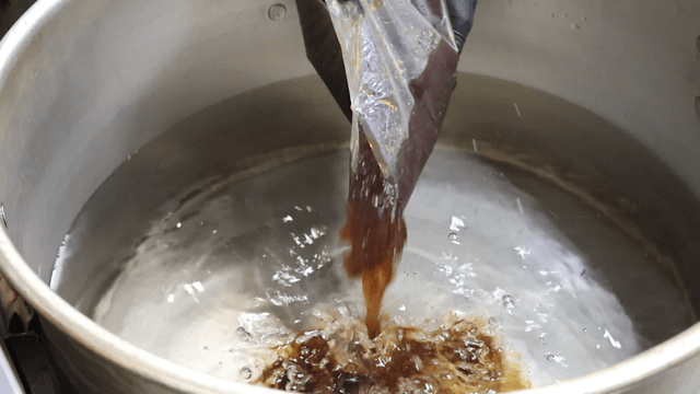 Dark broth being poured into large pot