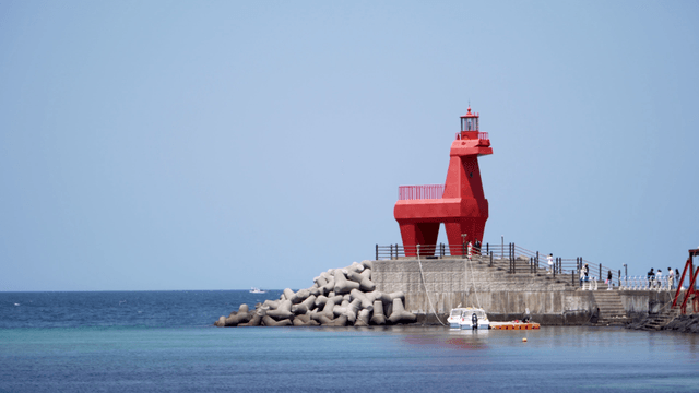 Red horse-shaped lighthouse by sea with people