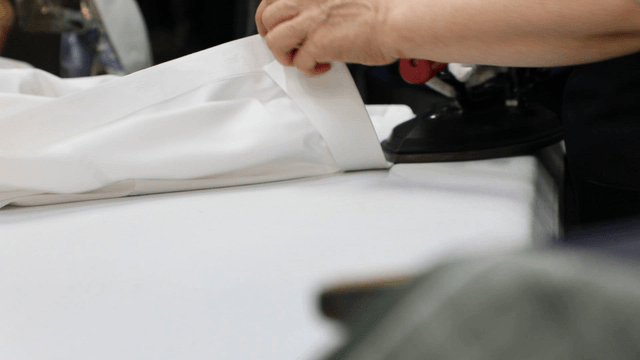 Hands ironing a white shirt on a table