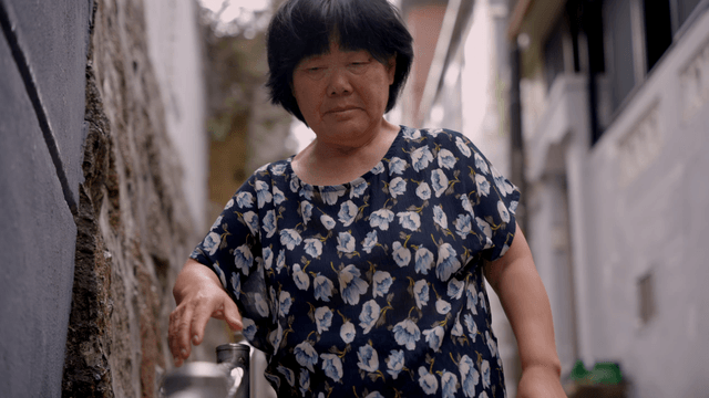 An elderly woman walking while holding a handrail