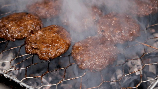 Grilled short rib patties sizzling on the rack