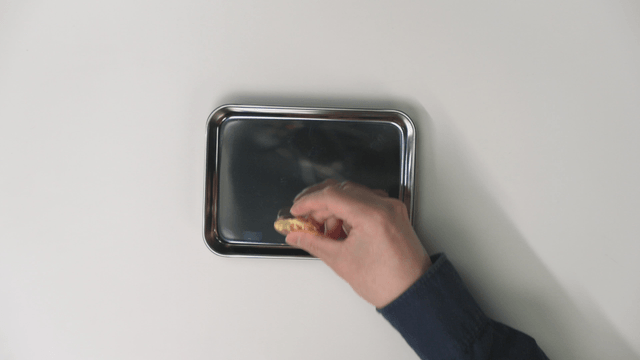 A hand picking up a bitcoin from a tray