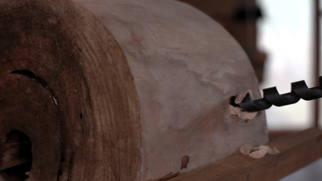 Spiral drill piercing a round wooden piece