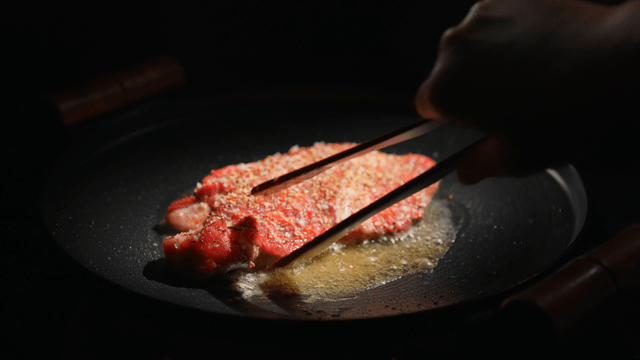 Steak sizzling in a pan with seasoning