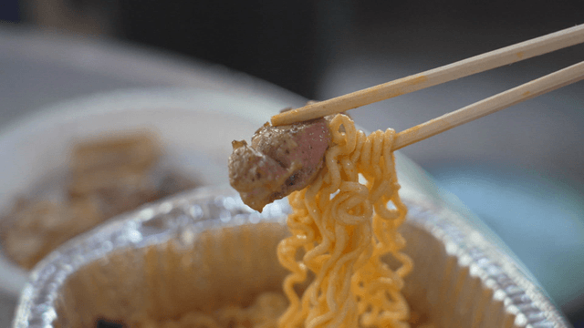 Wooden chopsticks holding ramen and pork belly
