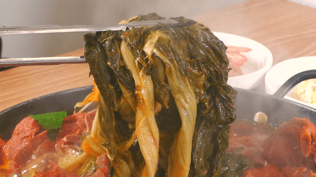 Tongs holding well-cooked outer leaves from pork back-bone stew